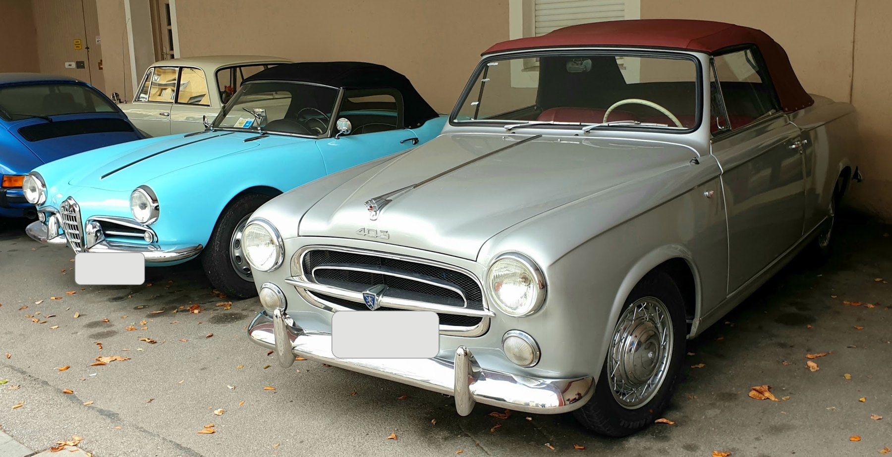 Ein silbernes Cabriolet aus den Fünfzigerjahren neben einem hellblauen italienischen Spider